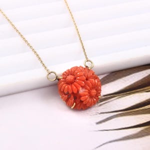 Pu&ograve; includere: Una collana con catena d'oro con un ciondolo in corallo intagliato con un gruppo di fiori rossi.