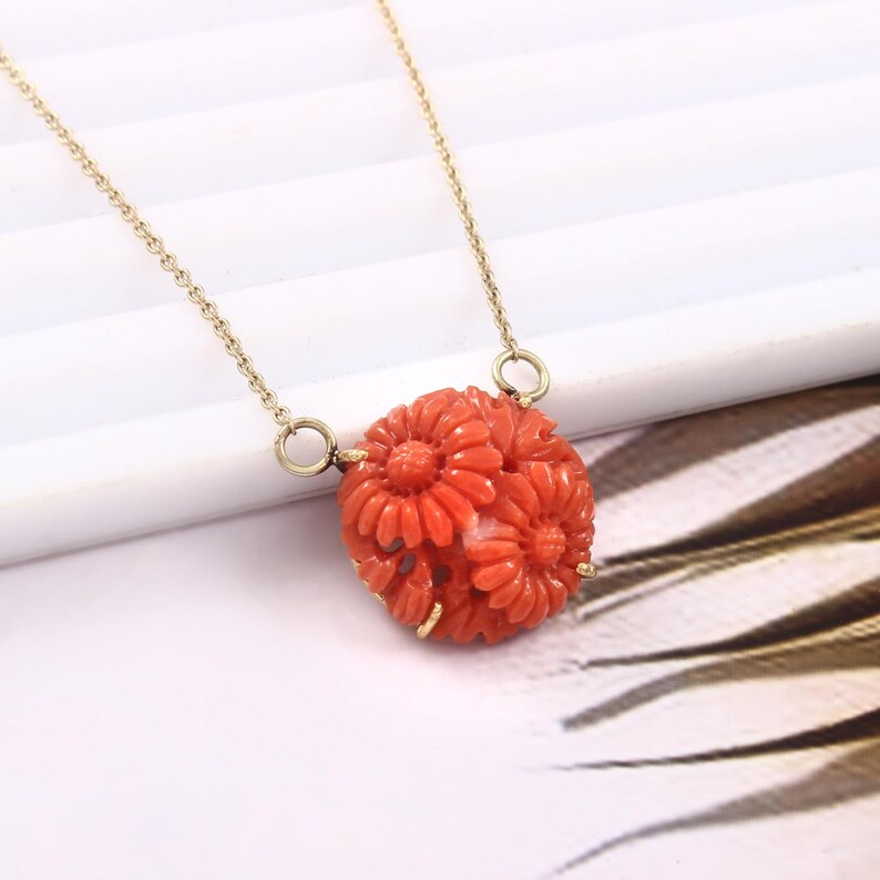 Pu&ograve; includere: Una collana con catena d'oro con un ciondolo in corallo intagliato con un gruppo di fiori rossi.