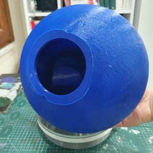 May include: A blue plastic sphere with a large circular opening. The sphere is sitting on a grey base.