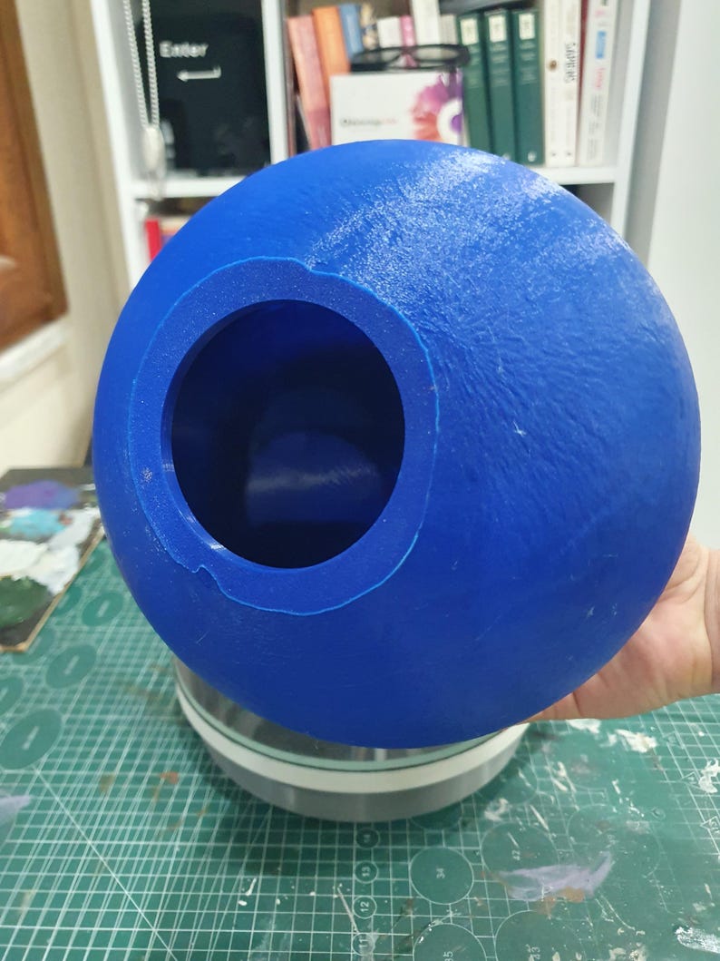 May include: A blue plastic sphere with a large circular opening. The sphere is sitting on a grey base.