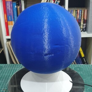 May include: A blue 3D printed sphere with white streaks on a white base. The sphere is on a rotating platform.