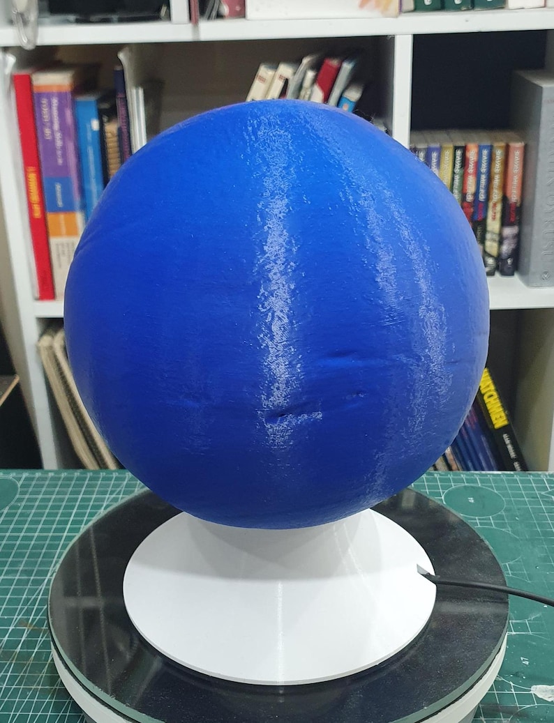 May include: A blue 3D printed sphere with white streaks on a white base. The sphere is on a rotating platform.