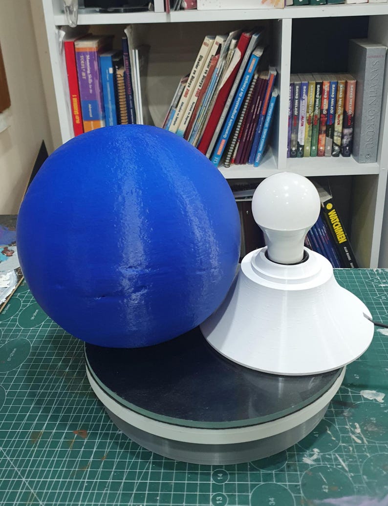 May include: A blue sphere sits on a black and white rotating platform. A white lamp base with a white light bulb sits on top of the sphere.