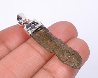 May include: A pendant featuring a rough-cut, olive-green gemstone with a silver-colored bail. The gemstone has a textured surface and irregular shape. The bail is stamped with the text "SilverForestaa".