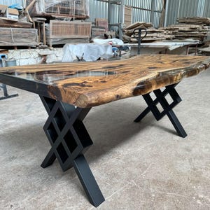 May include: A large wooden table with a live edge top and a clear epoxy finish. The table has a black metal base with a geometric design.