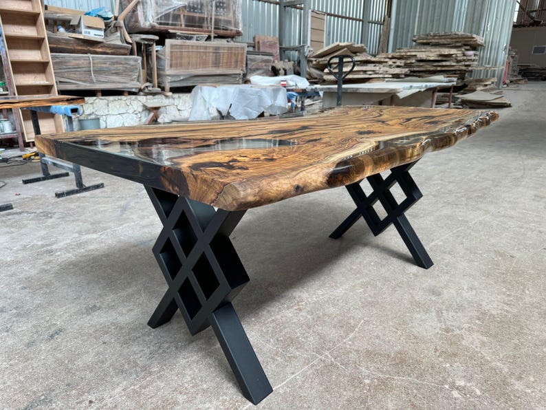 May include: A large wooden table with a live edge top and a clear epoxy finish. The table has a black metal base with a geometric design.
