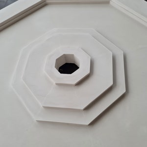 K&ouml;nnte beinhalten: Eine wei&szlig;e achteckige Deckenrosette mit einem konzentrischen Muster aus Achtecken. Die Rosette hat ein zentrales Loch.