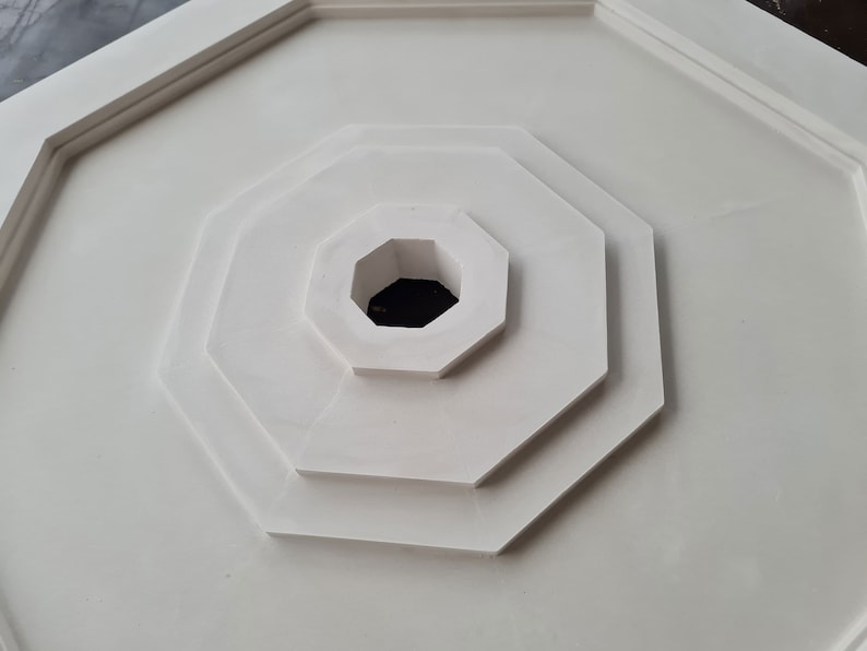K&ouml;nnte beinhalten: Eine wei&szlig;e achteckige Deckenrosette mit einem konzentrischen Muster aus Achtecken. Die Rosette hat ein zentrales Loch.
