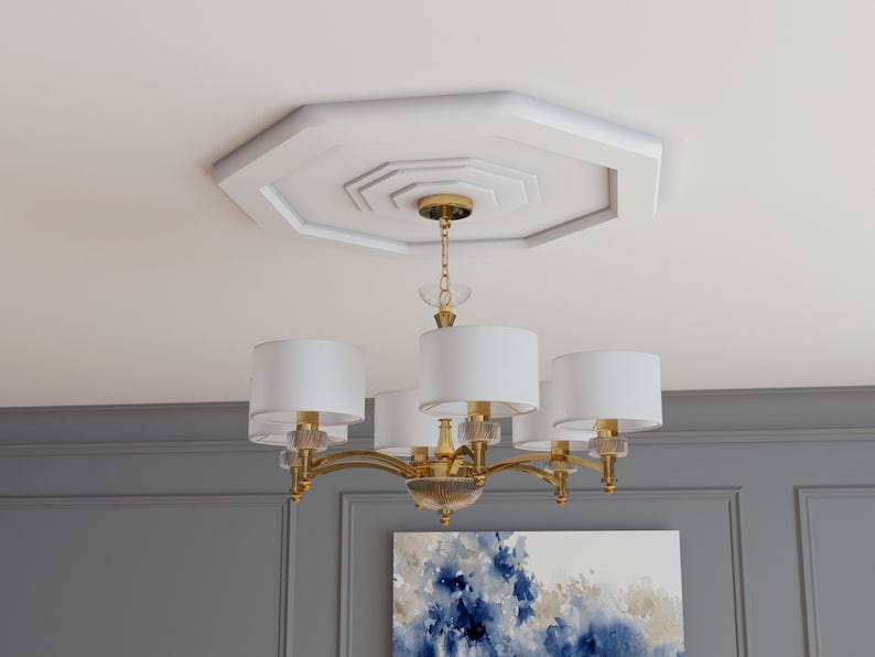K&ouml;nnte beinhalten: Ein goldener Kronleuchter mit wei&szlig;en Stoffschirmen h&auml;ngt an einem dekorativen achteckigen Deckenmedaillon. Der Kronleuchter hat sechs Lichter und ein geschwungenes Design.