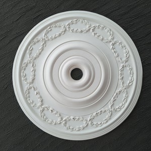 Könnte beinhalten: Weißer Deckenmedaillon mit einem dekorativen Rand aus Blättern und einem zentralen Kreis mit einem kleineren Kreis in der Mitte.