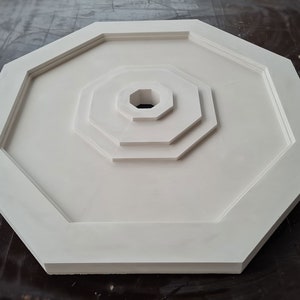 K&ouml;nnte beinhalten: Wei&szlig;es achteckiges Deckenmedaillon mit konzentrischem Kreisdesign. Das Medaillon hat eine glatte, matte Oberfl&auml;che.