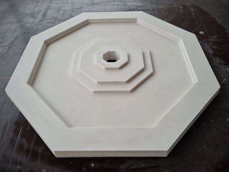 K&ouml;nnte beinhalten: Wei&szlig;es achteckiges Deckenmedaillon mit konzentrischem Kreisdesign. Das Medaillon hat eine glatte, matte Oberfl&auml;che.