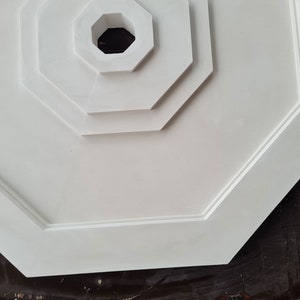 K&ouml;nnte beinhalten: Wei&szlig;er achteckiger Deckenmedaillon mit einem mehrschichtigen Design und einem zentralen Loch. Der Medaillon ist aus einem glatten, wei&szlig;en Material gefertigt.