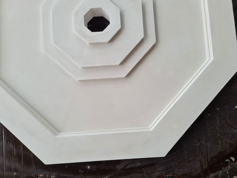K&ouml;nnte beinhalten: Wei&szlig;er achteckiger Deckenmedaillon mit einem mehrschichtigen Design und einem zentralen Loch. Der Medaillon ist aus einem glatten, wei&szlig;en Material gefertigt.