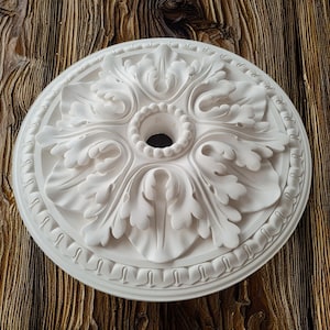 May include: White ceiling medallion with a decorative floral design. The medallion has a central hole for a light fixture.