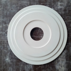 Pode incluir: Rosace de teto circular branca com três anéis concêntricos e um furo central.