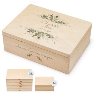 May include: A wooden keepsake box with a light wood finish. The lid features a watercolor design of green leaves and the text "Charlotte & Felix 18/08/2024" and "Unsere Erinnerungen". The box is available in two sizes: XL and M.
