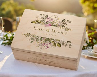 May include: A light-colored wooden box with a floral design and the names "Luisa & Marius" and the date "201012026" printed on the lid. The box is rectangular and sits on a white tablecloth.