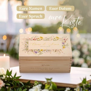 Op de afbeelding: Een lichtgekleurde houten kist met een bloemenontwerp en tekst. De kist heeft een rechthoekige vorm met een scharnierend deksel. Het deksel heeft een bloemstuk met de namen "Naomi & Simon" en de datum "2010.04.2026".