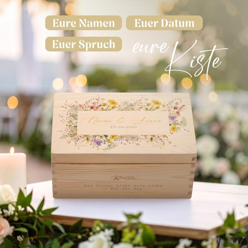 Op de afbeelding: Een lichtgekleurde houten kist met een bloemenontwerp en tekst. De kist heeft een rechthoekige vorm met een scharnierend deksel. Het deksel heeft een bloemstuk met de namen "Naomi & Simon" en de datum "2010.04.2026".
