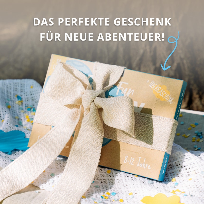 AMARI Kinder-Losbox, dekorativ mit einer Schleife auf einer Decke platziert – das perfekte Geschenk für neue Abenteuer.
