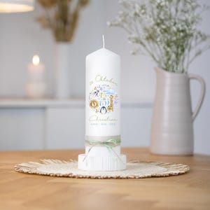 Könnte beinhalten: Eine weiße Säulenkerze mit dekorativem Design und dem Text "Oktober" und "It's a Boy". Die Kerze zeigt eine Giraffen-, Pinguin- und Sonnenillustration. Sie ist mit einem grünen Band gebunden und steht auf einem weißen Sockel.
