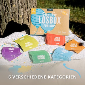 Ansicht der AMARI Losbox, präsentiert mit Losen in 6 Kategorien auf einem Tisch – viel Spaß für Kinder.