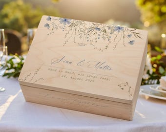 May include: A light-colored wooden box with a floral design and text. The box features a hinged lid with a watercolor-style floral pattern in blue and green. The text reads "Sina & Mattis, Hand in Hand, ein Leben lang, 16. August 2025."