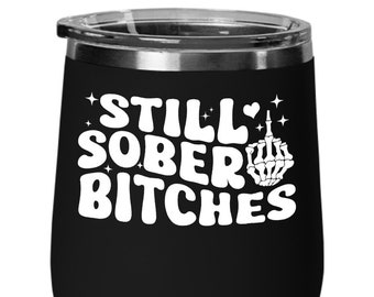 May include: Black stainless steel wine tumbler with a white graphic that says "Still Sober Bitches" with a skeleton middle finger.