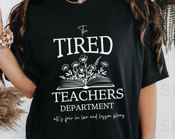 May include: Black t-shirt with white text that reads "The Tired Teachers Department all's fair in love and lesson plans". The text is surrounded by a floral design and an open book.