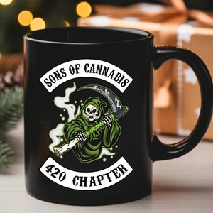 Pode incluir: Caneca de cerâmica preta com um desenho de ceifeiro segurando uma planta de cannabis e uma foice. A caneca tem o texto "SONS OF CANNABIS" acima da imagem e "420 CHAPTER" abaixo. O design é em verde, branco e preto.