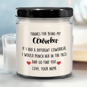 May include: A white candle jar with a black lid. The candle has a message that reads "Thanks for being my coworker. If I had a different coworker, I would punch her in the face and go find you. Love, your name."