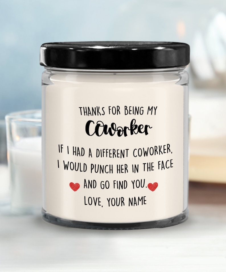 May include: A white candle jar with a black lid. The candle has a message that reads "Thanks for being my coworker. If I had a different coworker, I would punch her in the face and go find you. Love, your name."
