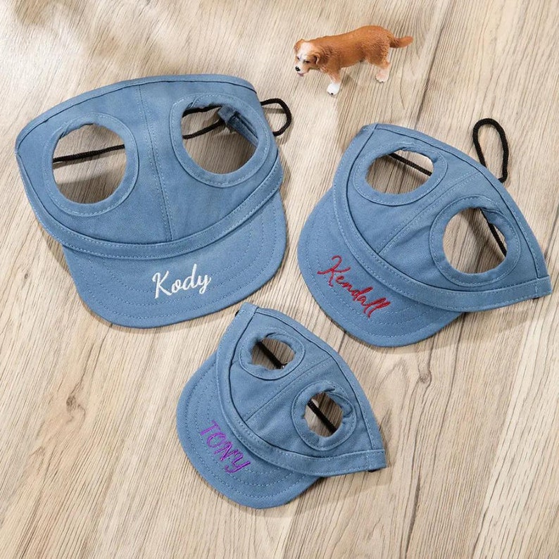 May include: Three blue denim dog hats with adjustable straps and two holes for the dog's ears. The hats are embroidered with the names "Kody", "Kendall", and "Tony".
