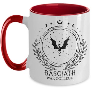 May include: White ceramic mug with a red interior and handle. The mug features a black dragon design within a circular frame, surrounded by stars, moons, and leaves. The text "BASGIATH WAR COLLEGE" is printed below the design.