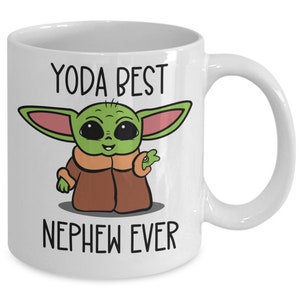 May include: White ceramic mug with a green, brown, and pink cartoon character with the text "YODA BEST NEPHEW EVER".