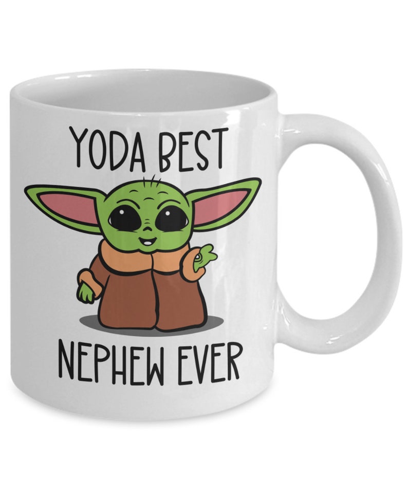 May include: White ceramic mug with a green, brown, and pink cartoon character with the text "YODA BEST NEPHEW EVER".
