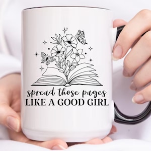 Puede incluir: Taza de cerámica blanca con asa y borde negros. La taza presenta una ilustración en blanco y negro de un libro con flores y mariposas. El texto "spread those pages like a good girl" está impreso en la taza.