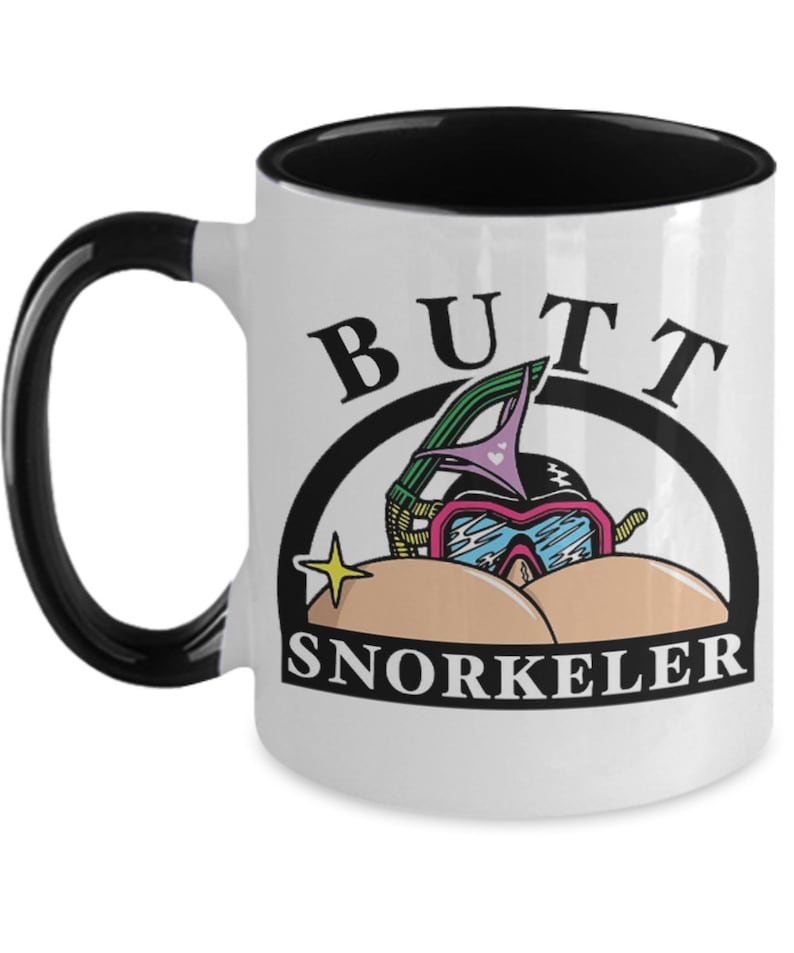 May include: White ceramic mug with a black handle and interior. The mug features a cartoon graphic of a snorkeling mask and the words "BUTT SNORKELER" in black text.