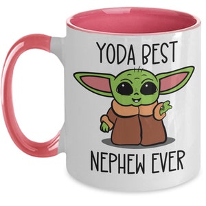 May include: White ceramic coffee mug with a pink rim and handle. The mug features a cartoon image of a green Baby Yoda character with the text "Yoda Best Nephew Ever".