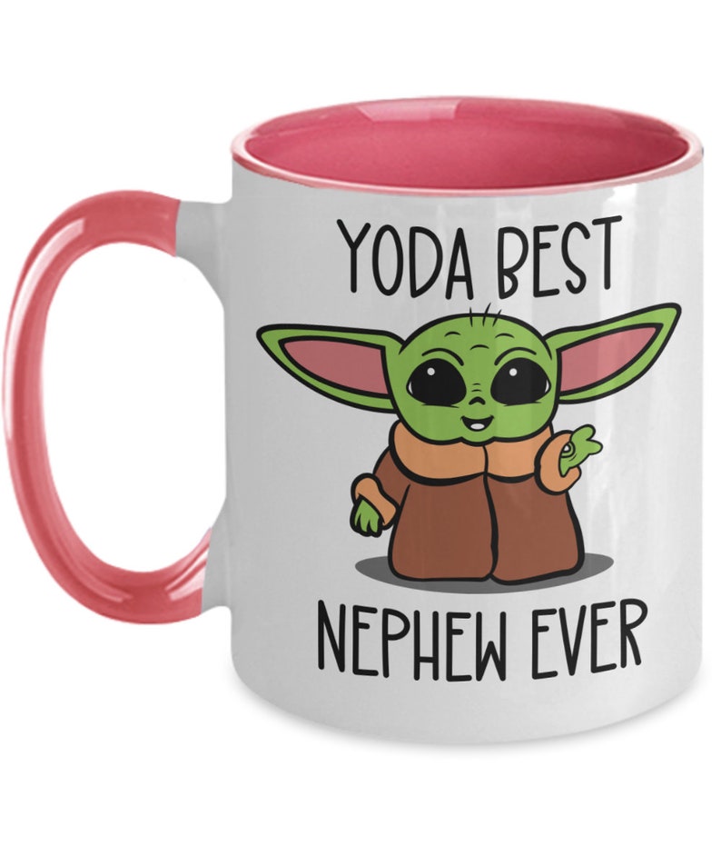 May include: White ceramic coffee mug with a pink rim and handle. The mug features a cartoon image of a green Baby Yoda character with the text "Yoda Best Nephew Ever".