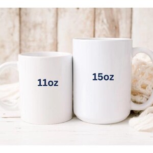 May include: Two white ceramic mugs. The smaller mug has "11oz" printed on it in navy blue. The larger mug has "15oz" printed on it in navy blue. Both mugs have a handle and are set against a neutral background.
