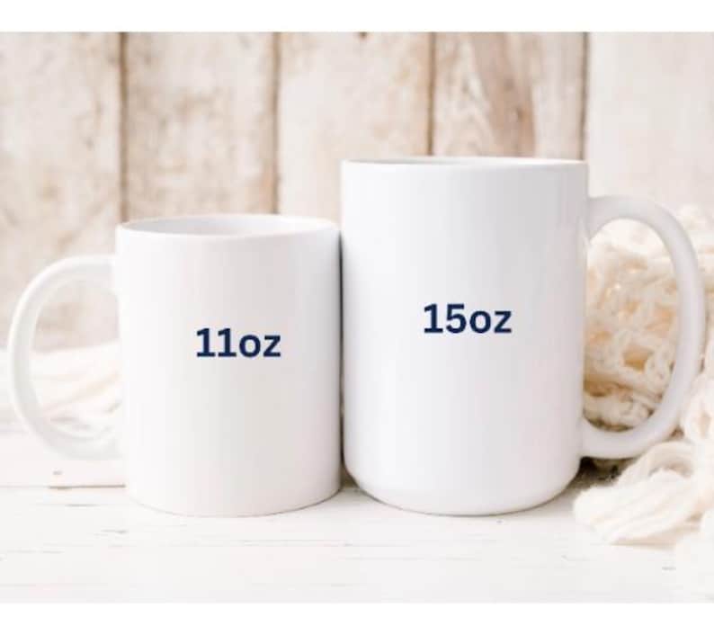 May include: Two white ceramic mugs. The smaller mug has "11oz" printed on it in navy blue. The larger mug has "15oz" printed on it in navy blue. Both mugs have a handle and are set against a neutral background.
