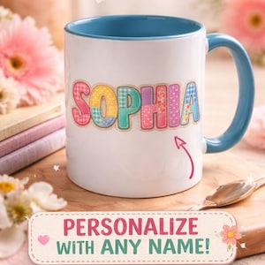 Pode incluir: Caneca de cerâmica branca com interior e alça azuis. O nome "SOPHIA" é exibido em letras coloridas e estampadas. A caneca é decorada com uma seta rosa e o texto "PERSONALIZE COM QUALQUER NOME!"