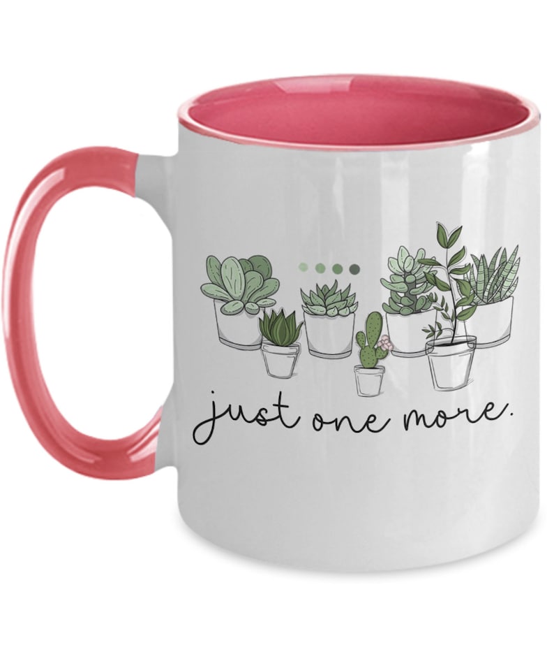 May include: White ceramic coffee mug with a pink rim and handle. The mug features a line drawing of potted succulents with the text "just one more."