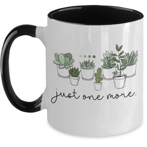 May include: White ceramic coffee mug with a black interior and handle. The mug features a line drawing of potted succulents with the text "just one more."