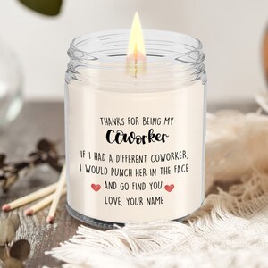 May include: A clear glass candle jar with a white candle inside. The candle has a label that reads "Thanks for being my coworker. If I had a different coworker, I would punch her in the face and go find you. Love, your name."