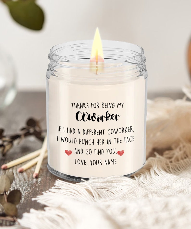 May include: A clear glass candle jar with a white candle inside. The candle has a label that reads "Thanks for being my coworker. If I had a different coworker, I would punch her in the face and go find you. Love, your name."
