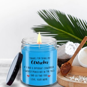 May include: A blue candle in a glass jar with a black lid. The candle has a white label with the text "THANKS FOR BEING MY Coworker IF I HAD A DIFFERENT COWORKER, I WOULD PUNCH HER IN THE FACE AND GO FIND YOU. LOVE, YOUR NAME".