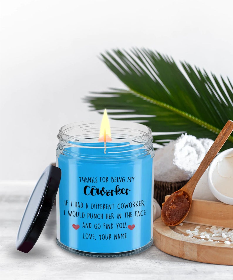 May include: A blue candle in a glass jar with a black lid. The candle has a white label with the text "THANKS FOR BEING MY Coworker IF I HAD A DIFFERENT COWORKER, I WOULD PUNCH HER IN THE FACE AND GO FIND YOU. LOVE, YOUR NAME".
